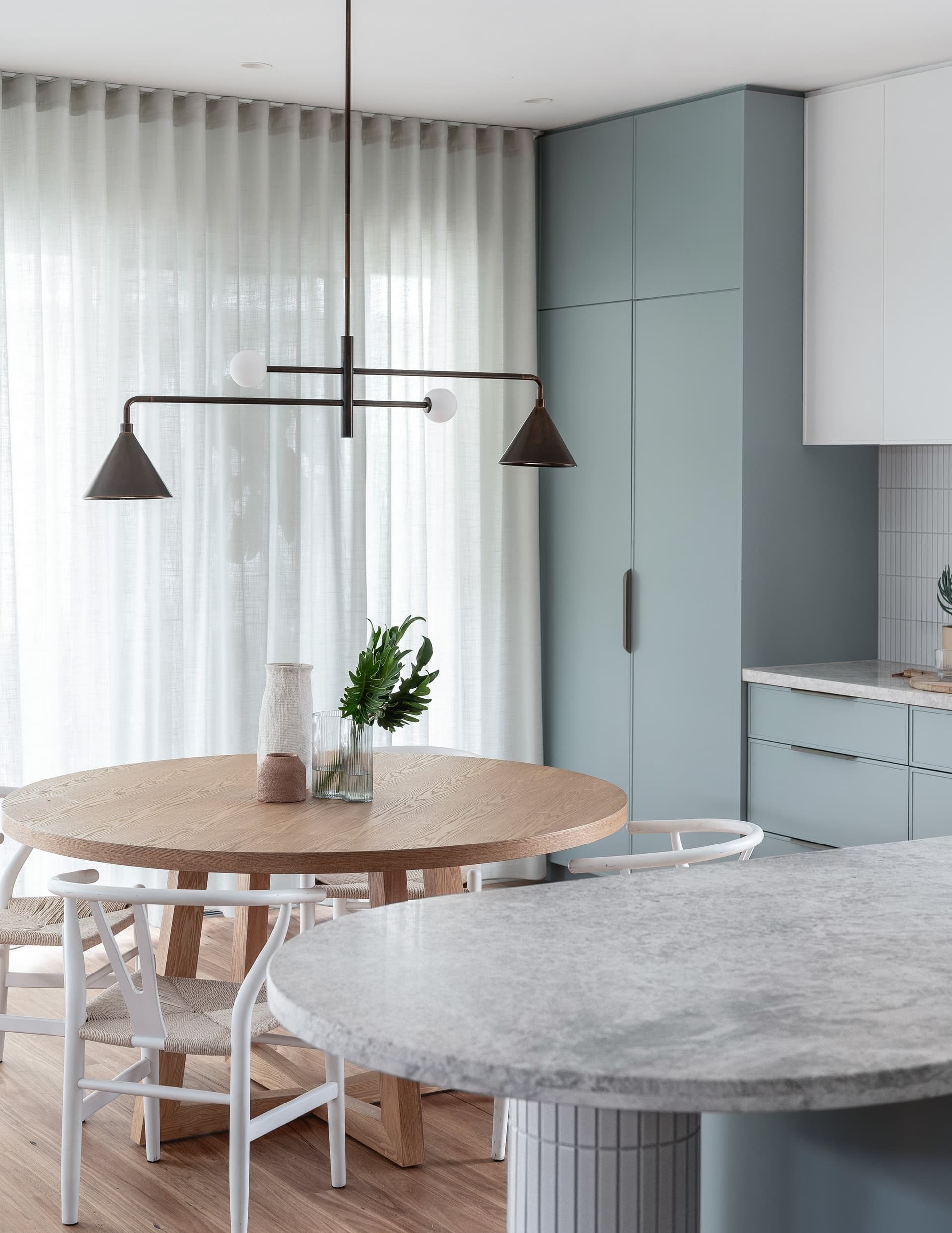 Round timber dining table under a linear pendant
